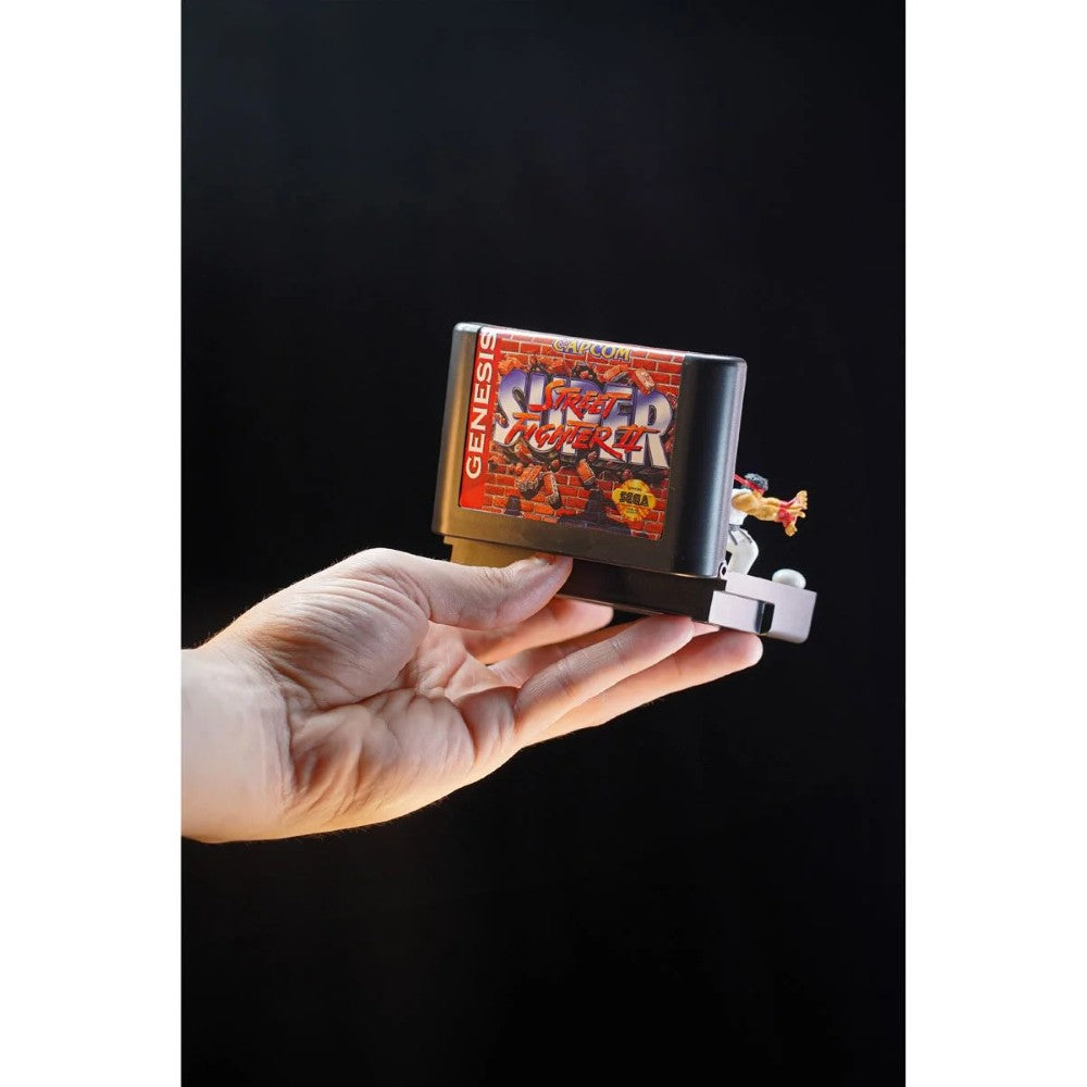 Hand holding Console Heroes Sega Genesis Genesis Street Fighter II Cartridge Diorama Playset collectible with miniature figure detail.