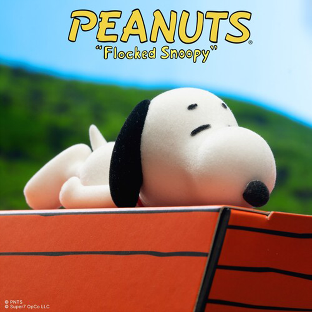 Flocked Snoopy plush resting on a red doghouse beneath the Peanuts logo