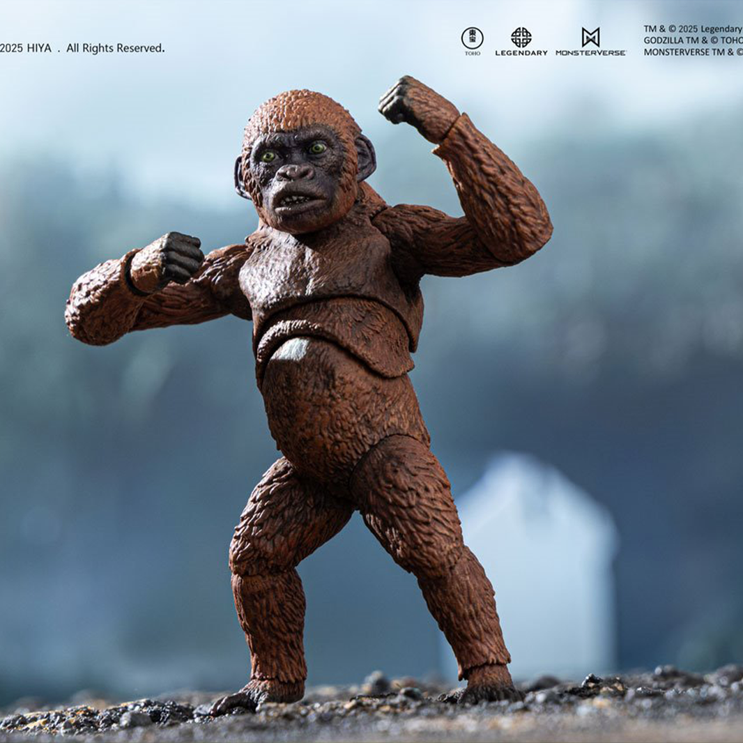 Articulated gorilla figure with textured brown fur and green eyes posed with raised fists on rocky surface against blurred background