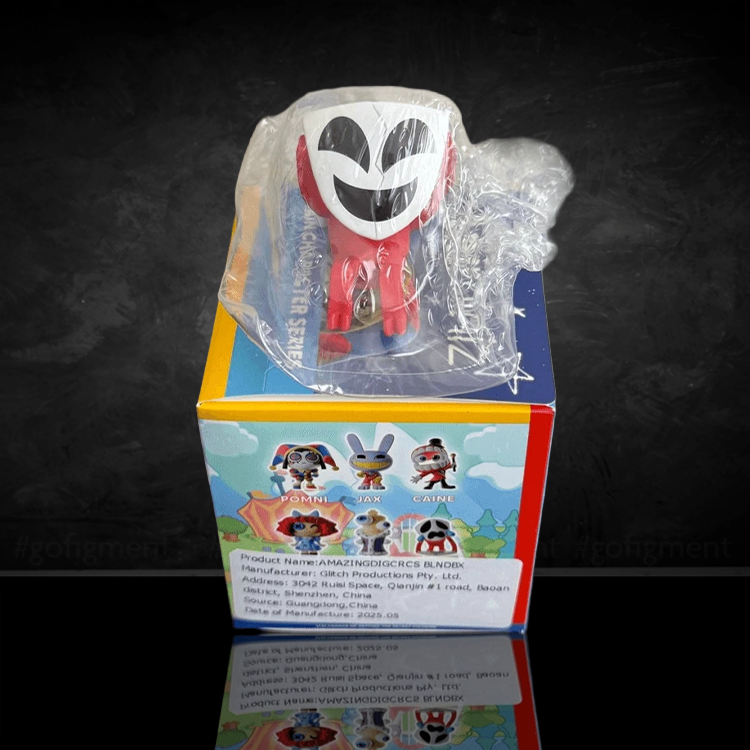 Small red and white vinyl figure with a smiling face wrapped in plastic, sitting on a colorful collectible box with character images.