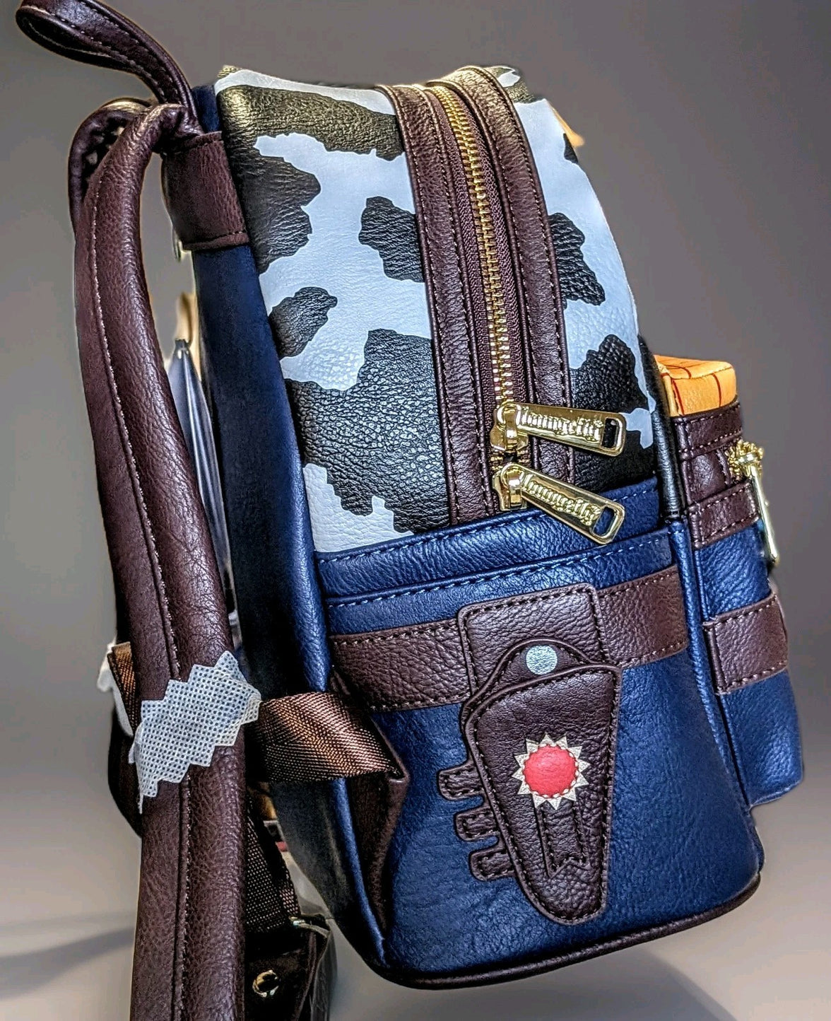 Side view of Loungefly Toy Story mini backpack with cow print, brown straps, and sheriff badge detail