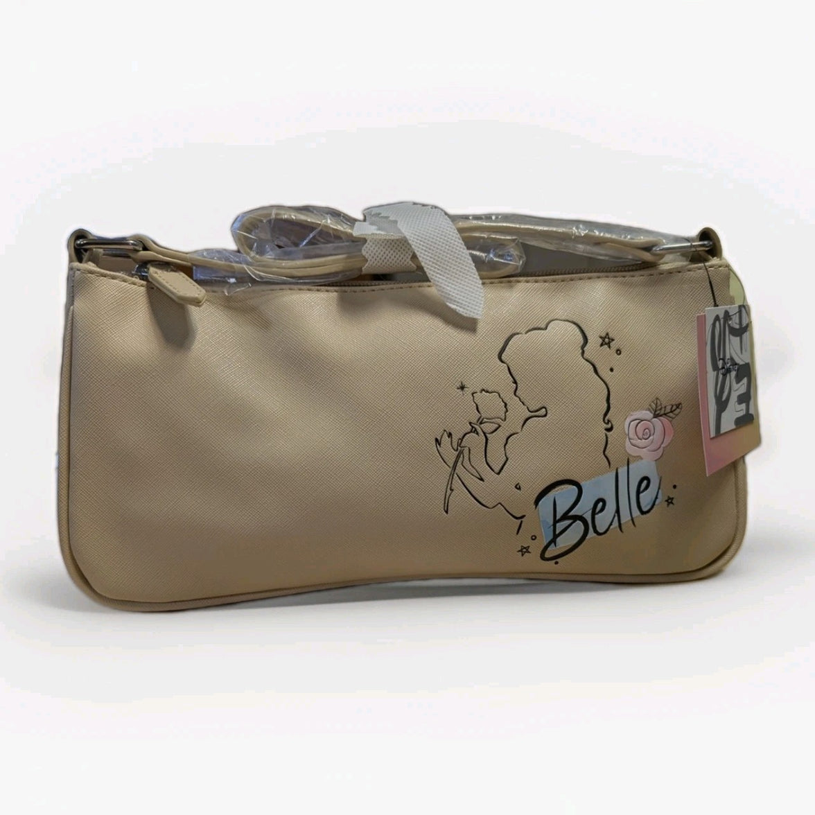 Danielle Nicole beige crossbody bag with Belle silhouette holding rose and decorative script on textured surface