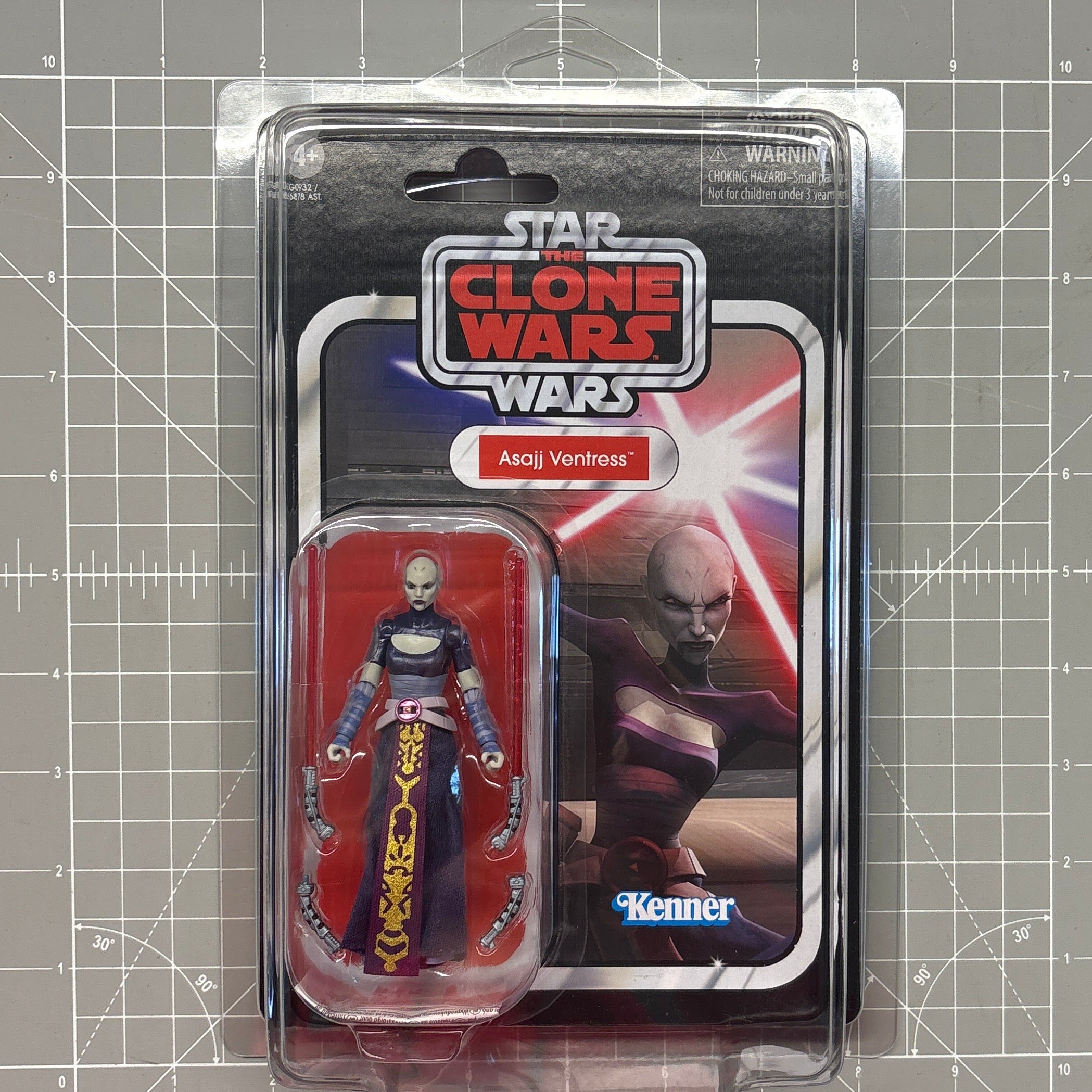 Packaged Star Wars The Clone Wars Asajj Ventress action figure on a gridded cutting mat