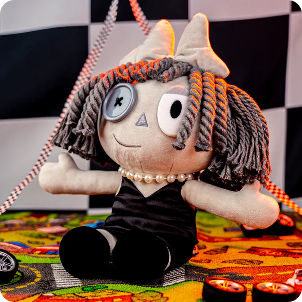 Glitch Ragatha Noir plush doll in black dress with button eye and yarn hair sitting on colorful patterned surface