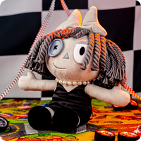Glitch Ragatha Noir plush doll in black dress with button eye and yarn hair sitting on colorful patterned surface