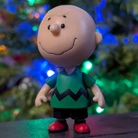 Loose Super7 Charlie Brown figure in green zigzag shirt standing with colorful holiday lights softly glowing behind him