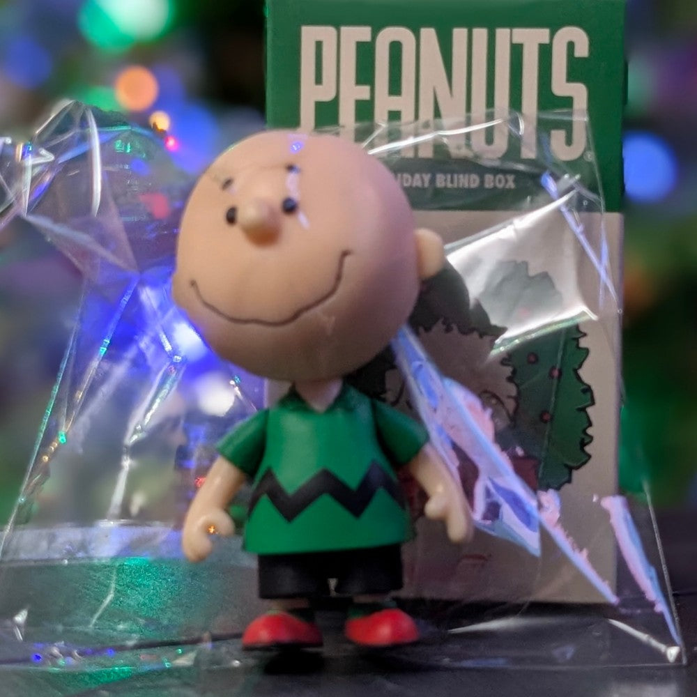Super7 loose Charlie Brown figure in green zigzag shirt standing in front of Peanuts Holiday Blind Box packaging