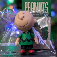 Super7 loose Charlie Brown figure in green zigzag shirt standing in front of Peanuts Holiday Blind Box packaging