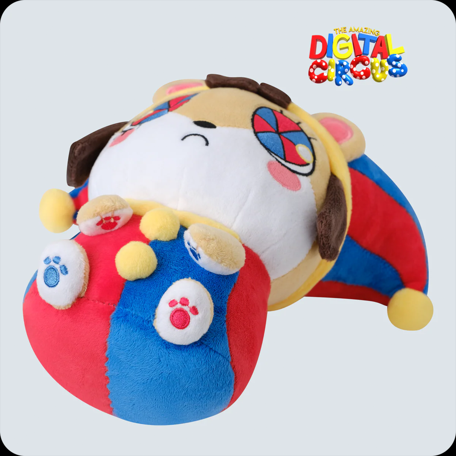 Plush toy of a colorful jester hamster with patchwork eyes, lying on a red and blue ball against a light background.