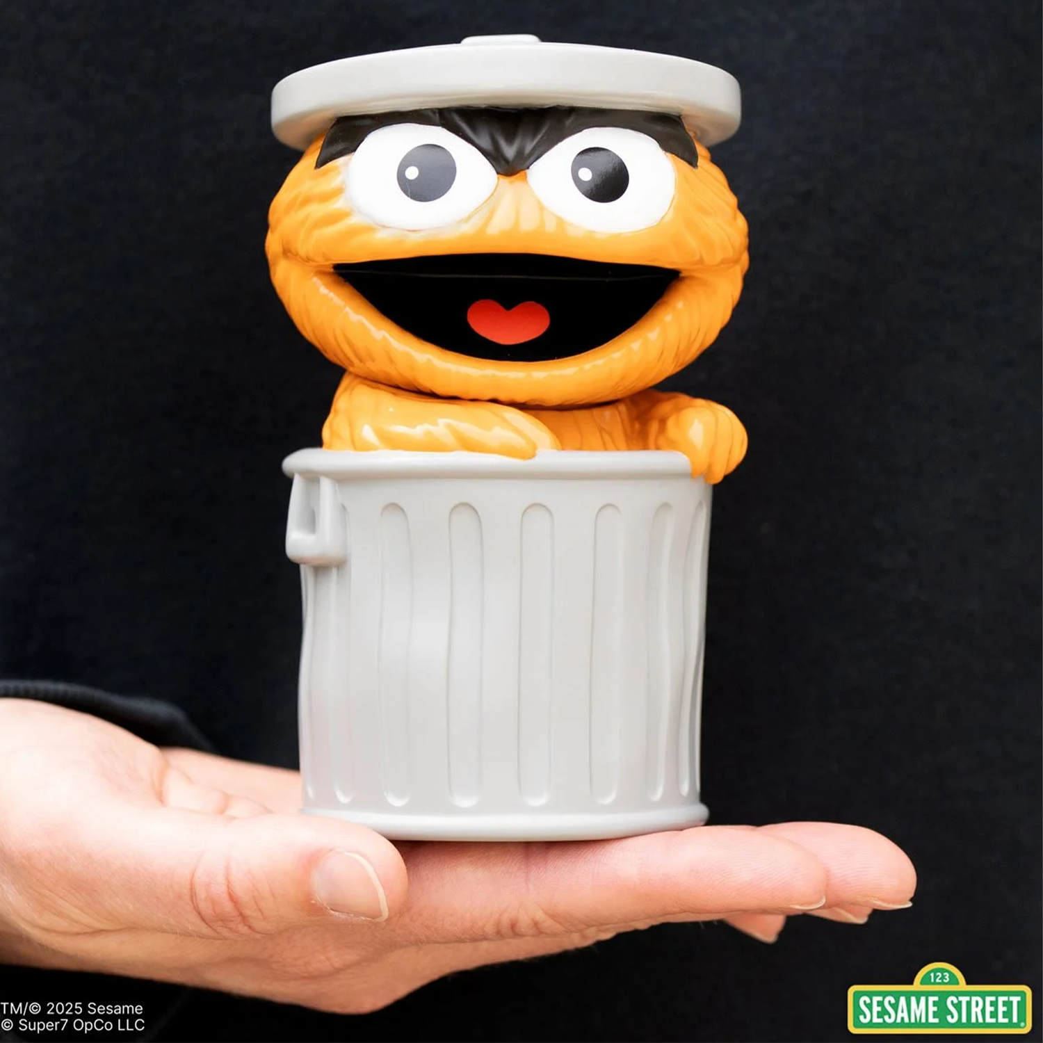Sesame Street Oscar the Grouch (Orange) FUN! FUN! Vinyl Figure sitting in a silver trash can held in a hand against black background