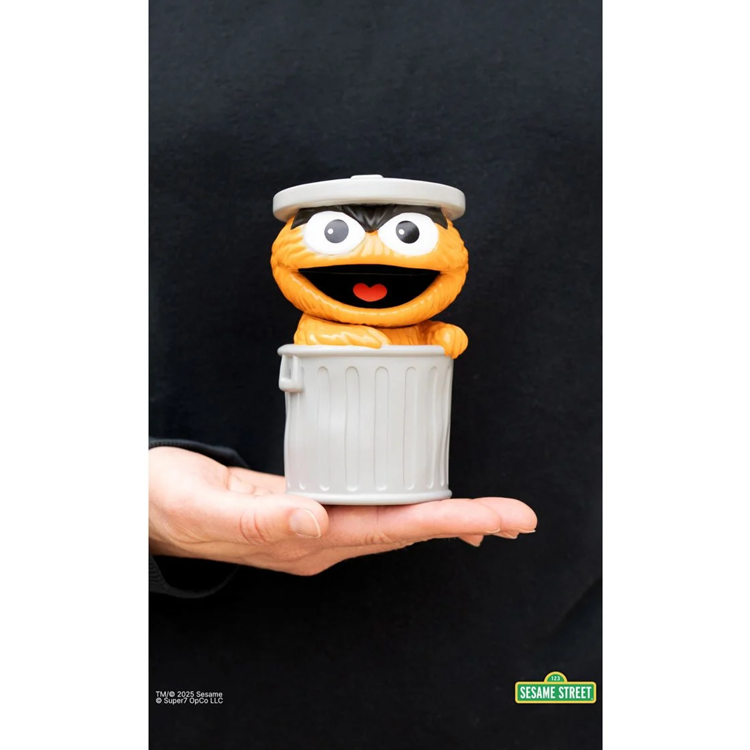 Sesame Street Oscar the Grouch (Orange) FUN! FUN! Vinyl Figure held in hand with trash can lid on head against black background
