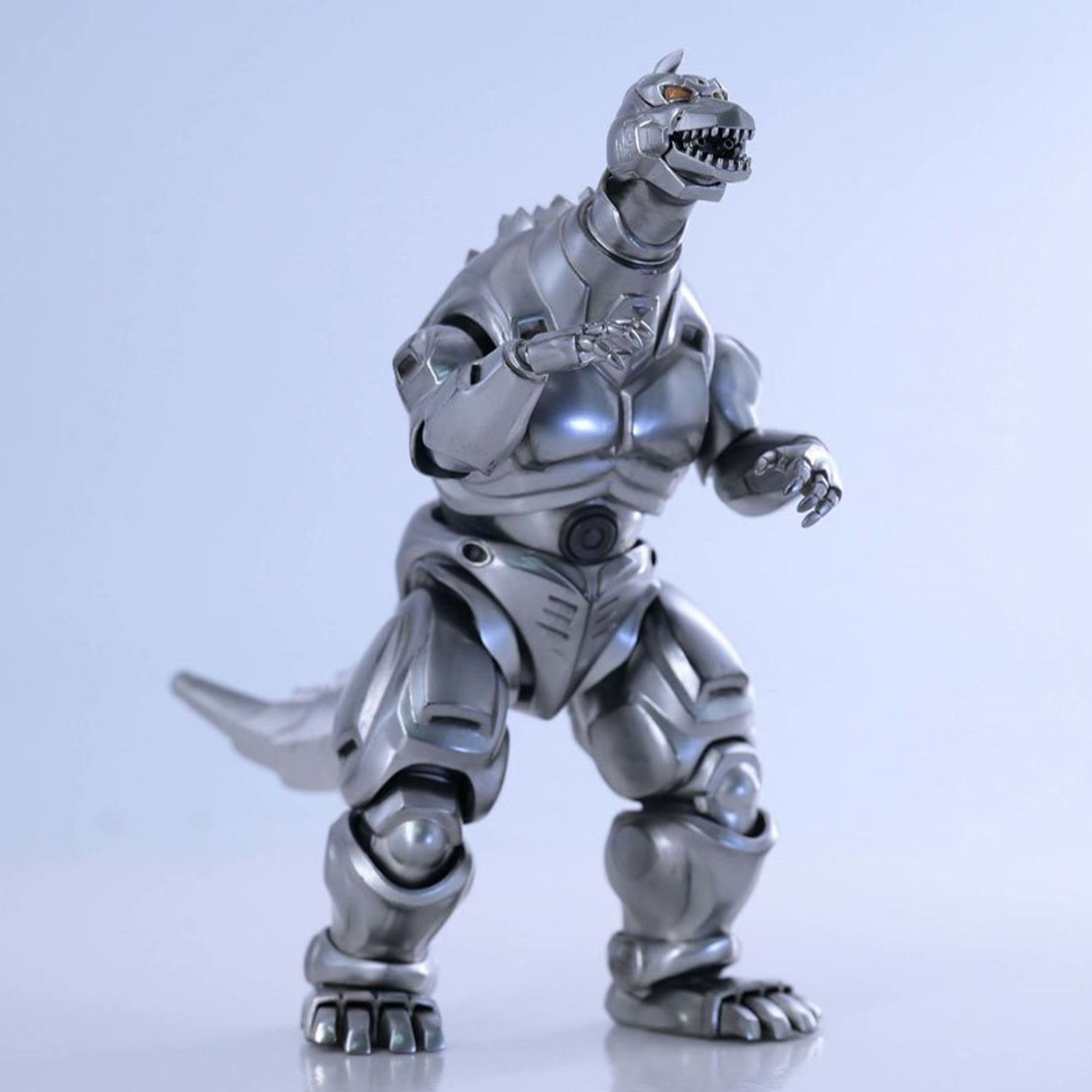 Articulated silver robot dinosaur figure with glowing eyes and detailed mechanical armor posed on smooth reflective surface
