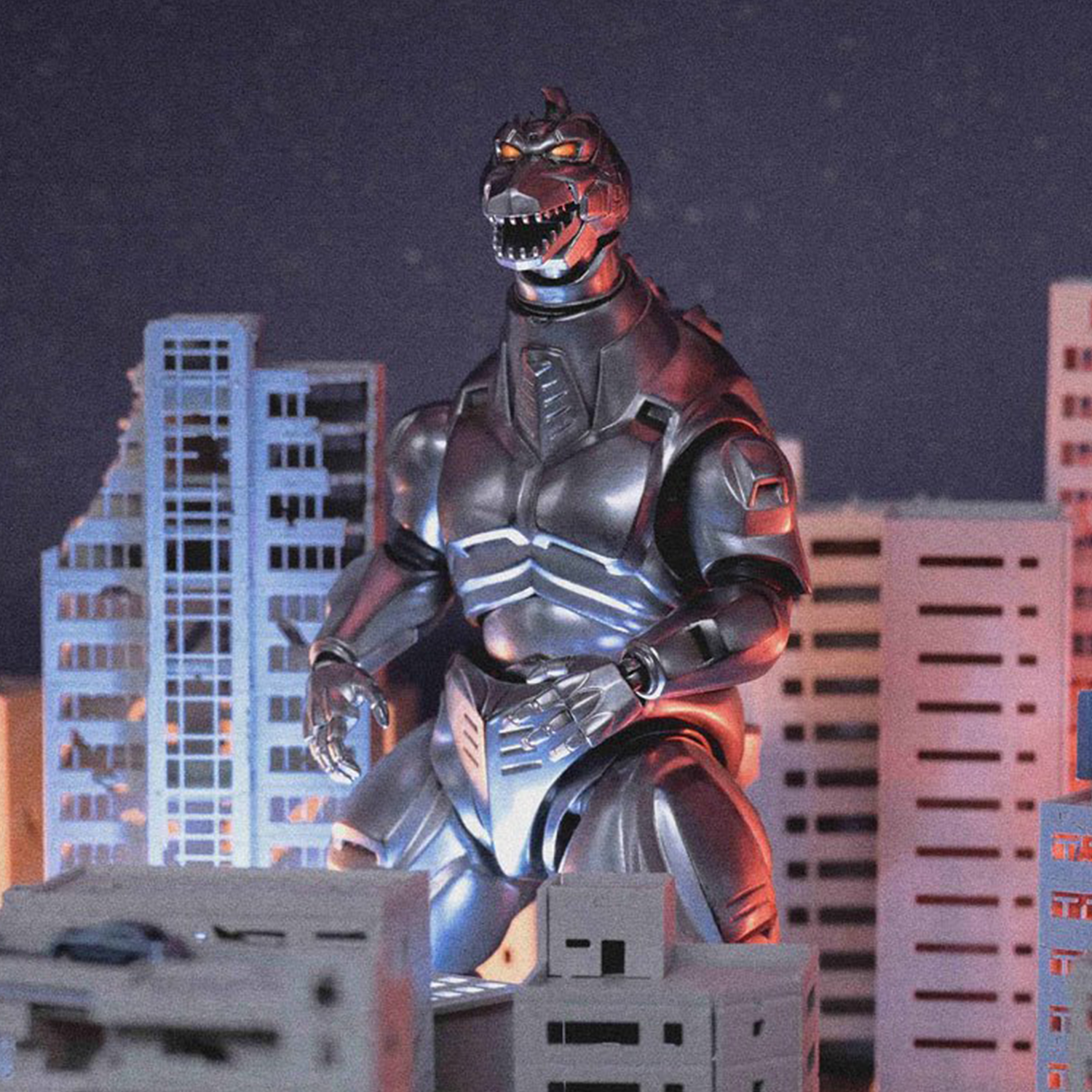 Dark metallic Mechagodzilla figure with illuminated eyes standing amid miniature city buildings at night.