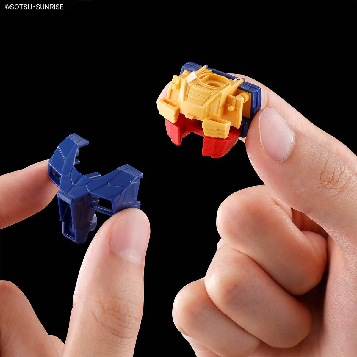Close-up of hands holding small blue and yellow plastic model parts against a black background
