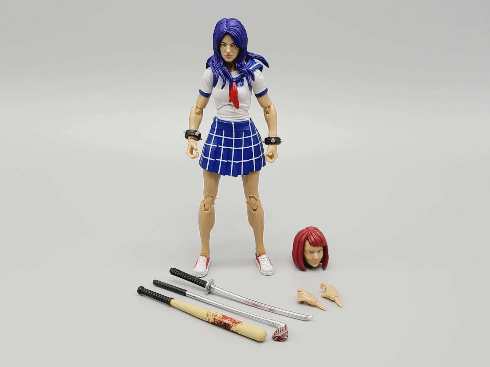 Action figure with blue hair and school uniform standing next to additional accessories on a gray background