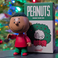 Loose Franklin Peanuts holiday ReAction figure in red and green with Super7 festive blind box and blurred lights background