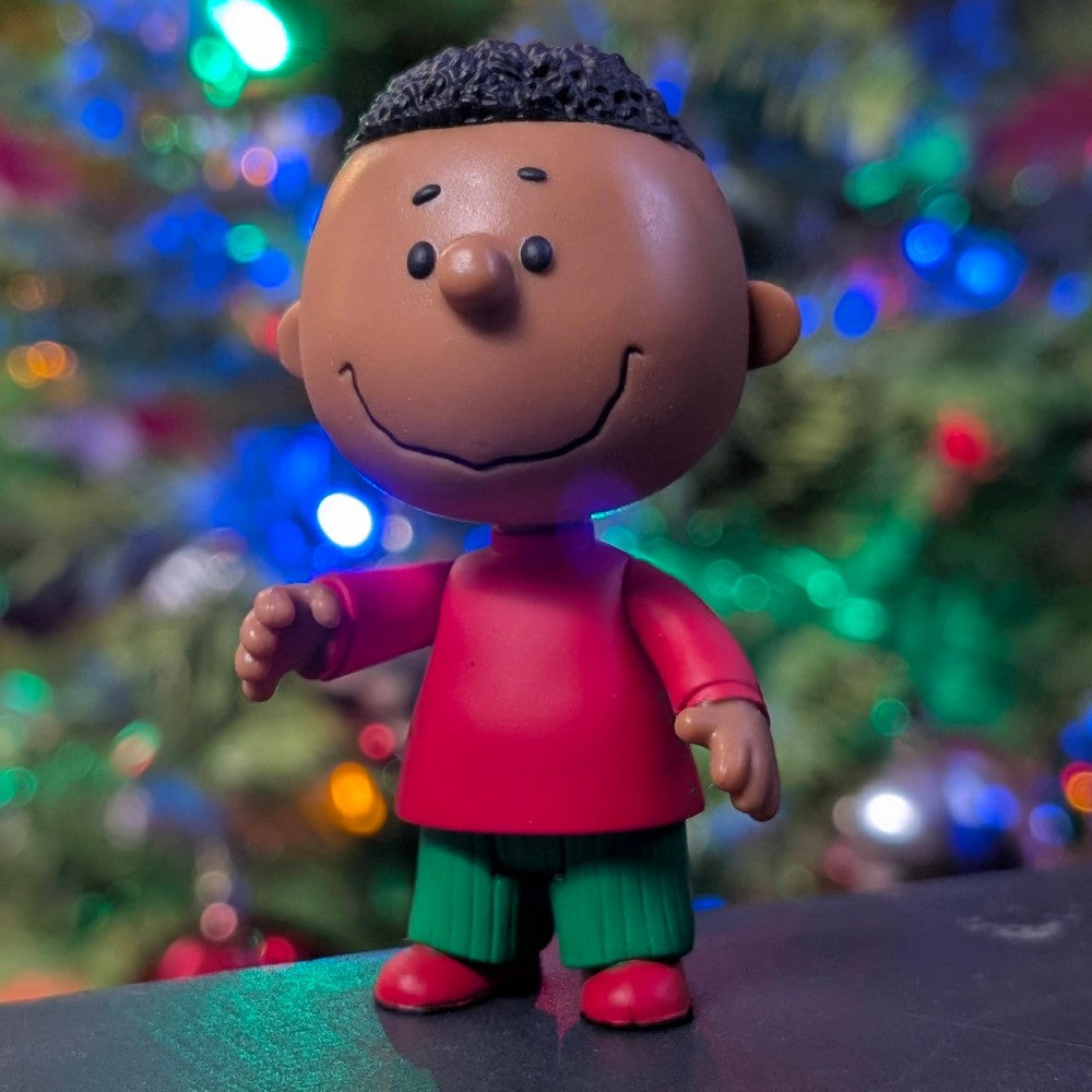 Super7 Franklin figure in red shirt and green pants with smiling face and festive colorful lights background