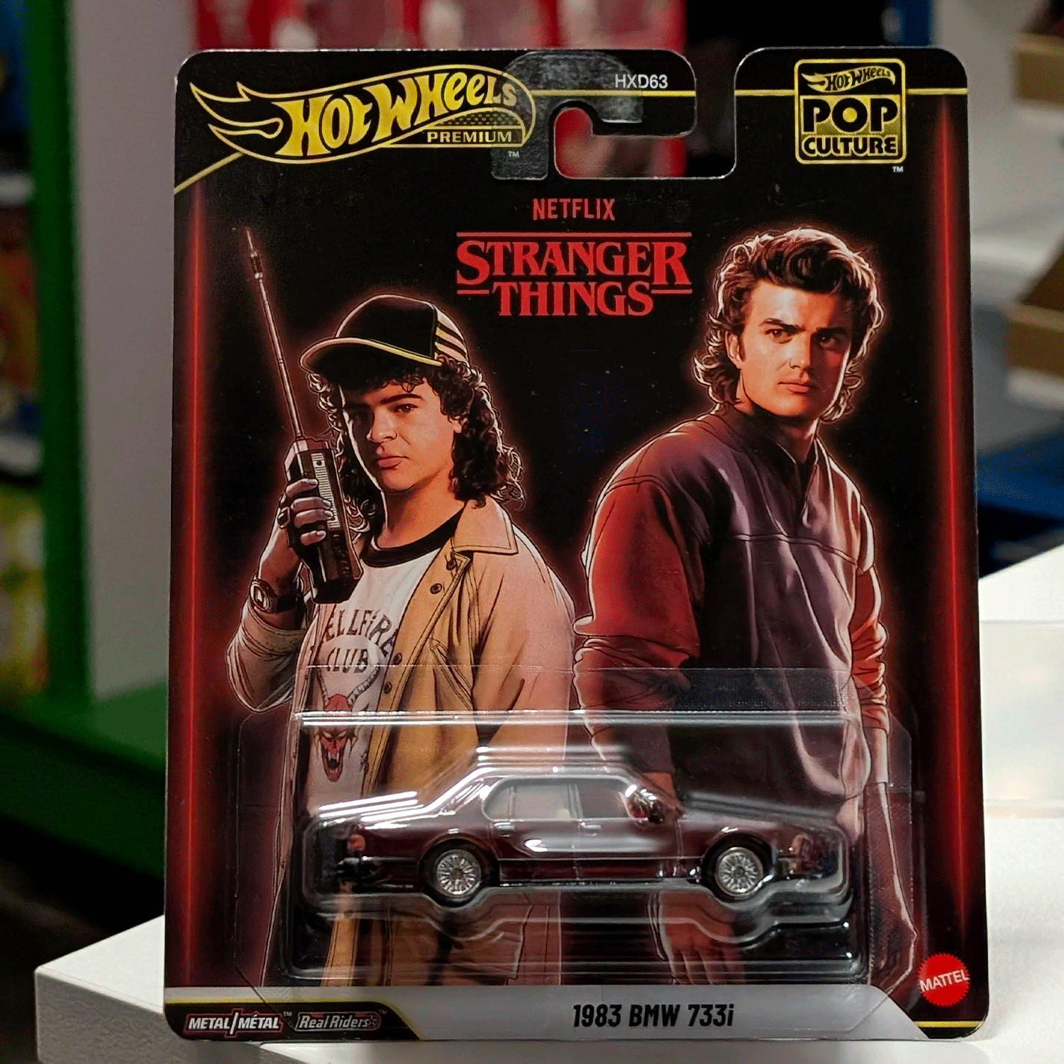Mattel Hot Wheels 1983 BMW 733i Stranger Things Pop Culture 2026 die-cast car with character art packaging front view