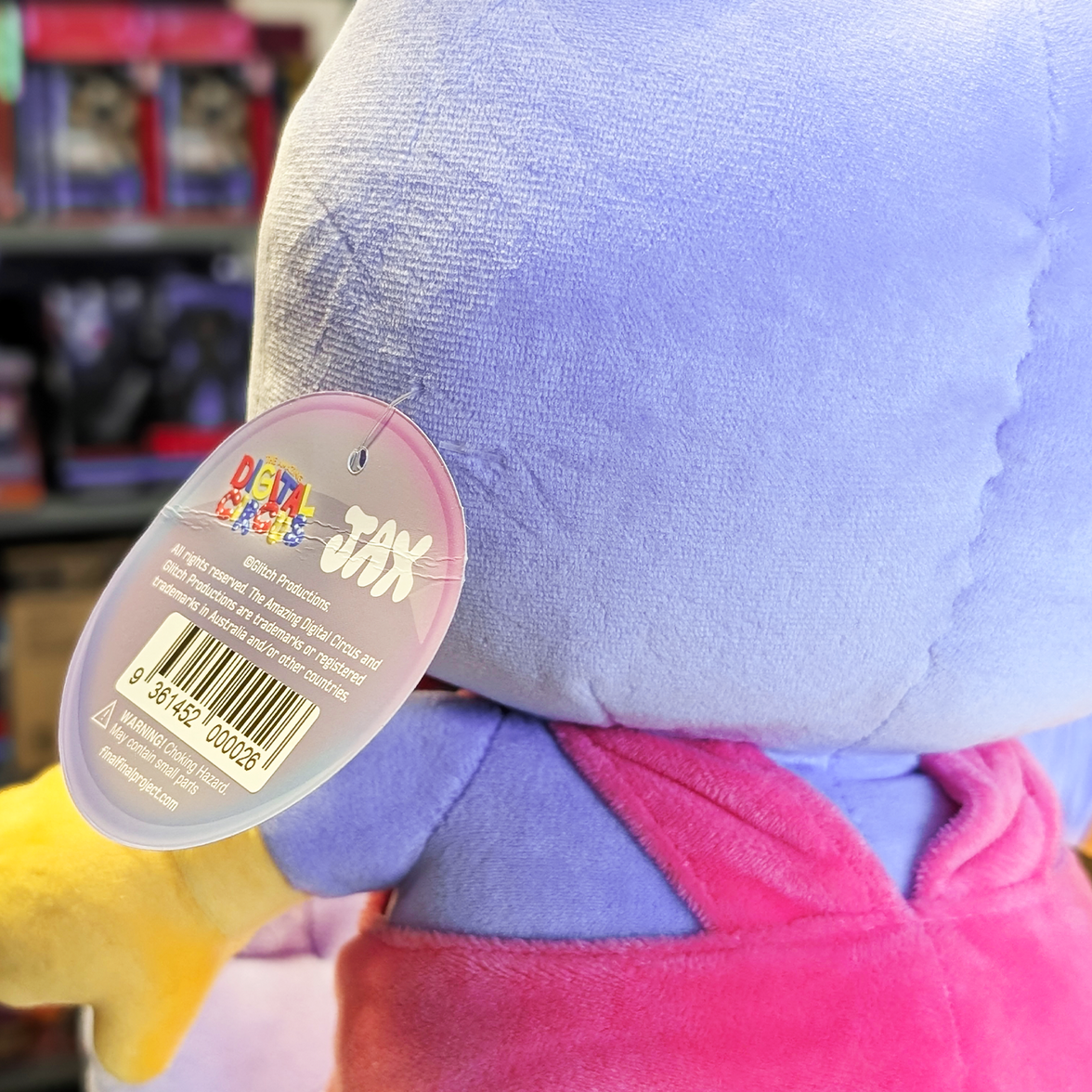 Close-up of Glitch tag attached to the back of purple and pink Jax plush toy from The Amazing Digital Circus collection