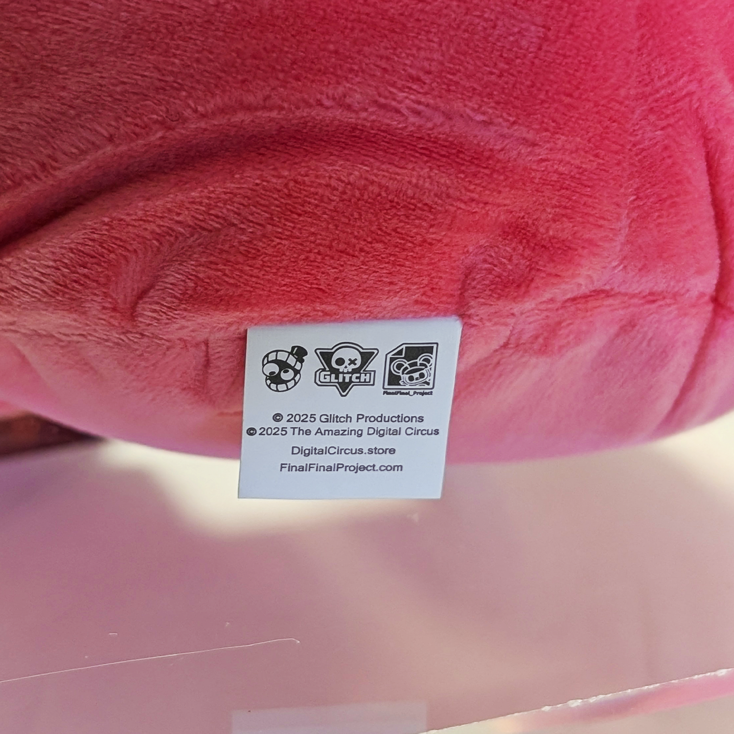 Close-up of Glitch branded tag on pink plush toy from The Amazing Digital Circus collectible series