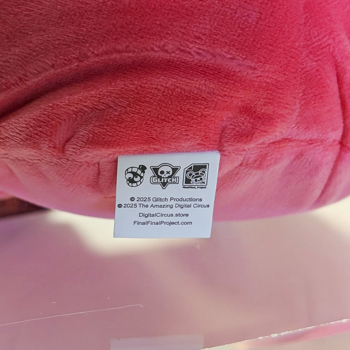 Close-up of Glitch branded tag on pink plush toy from The Amazing Digital Circus collectible series