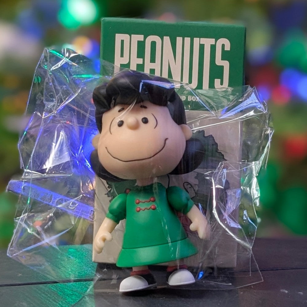 Super7 Peanuts Lucy VanPelt figure in green dress inside clear packaging with Peanuts box and festive lights background