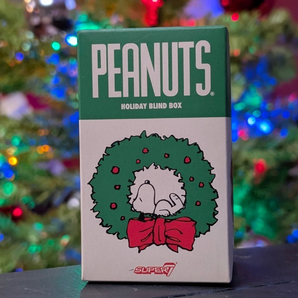 Super7 Peanuts Holiday Blind Box with Snoopy inside festive green wreath and red bow against colorful holiday lights background