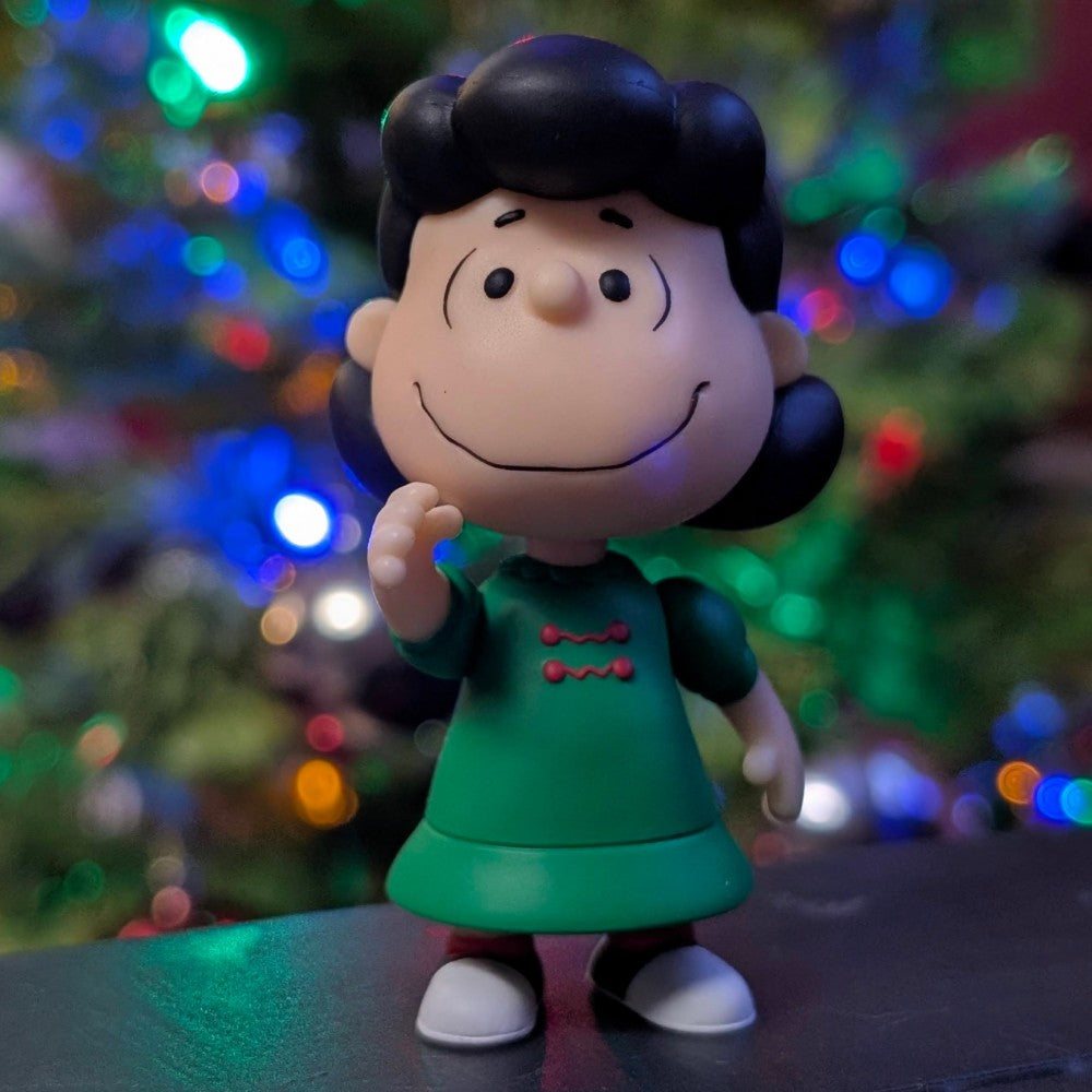 Loose Super7 Lucy Van Pelt figure in festive green dress with holiday lights and tree blurred background
