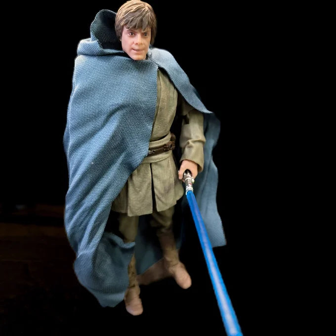 Luuke Last Command Star Wars Black Series 6-inch action figure holding blue lightsaber with fabric cloak isolated on black background