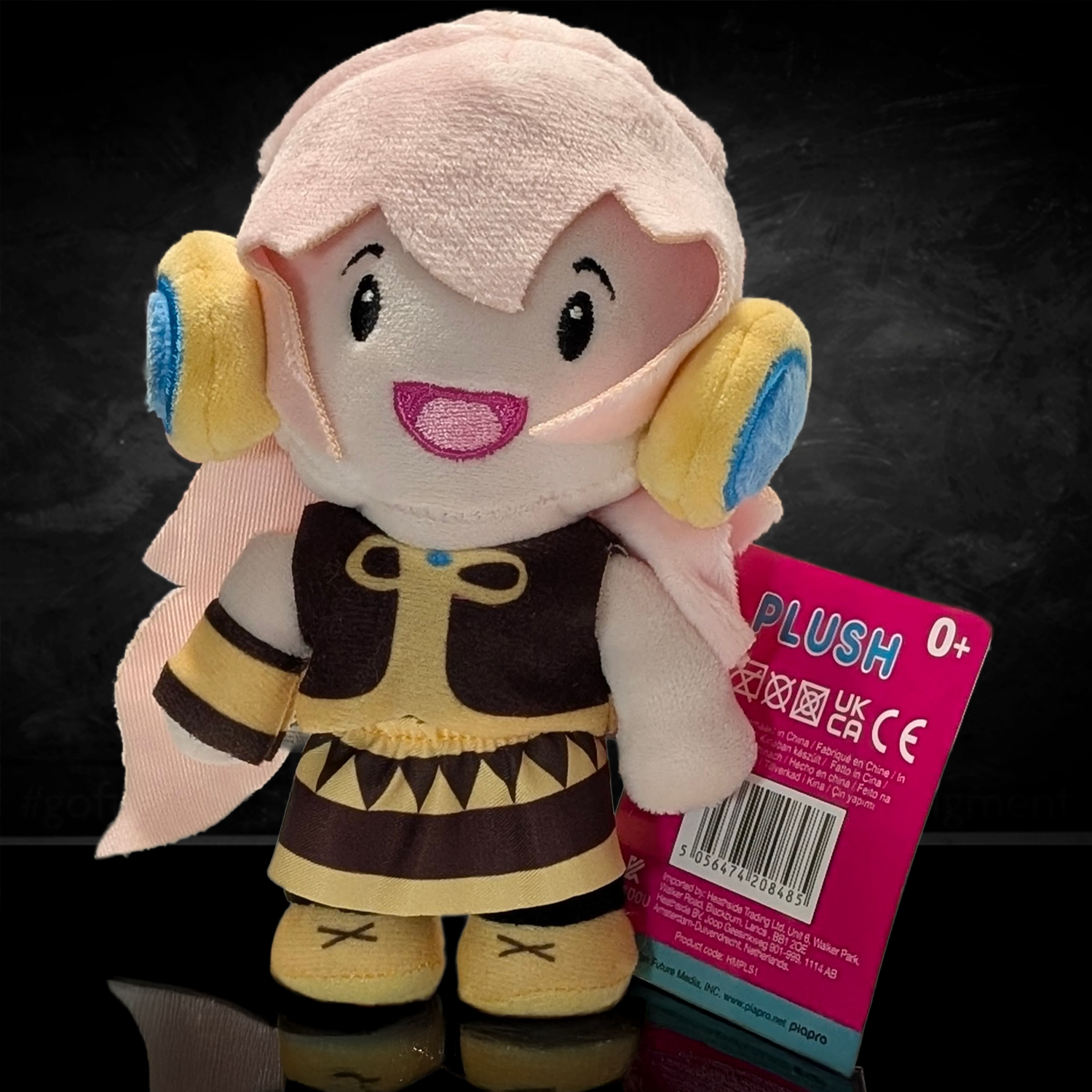 UCC 6-inch Megurine Luka plush with pink hair, yellow and blue headphones, wearing brown outfit and holding product tag