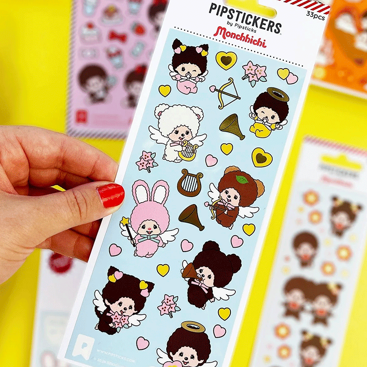 Hand holding PipSticks Monchhichi PVC sticker sheet with cute angel and heart designs on blue background
