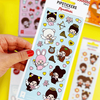Hand holding PipSticks Monchhichi PVC sticker sheet with cute angel and heart designs on blue background