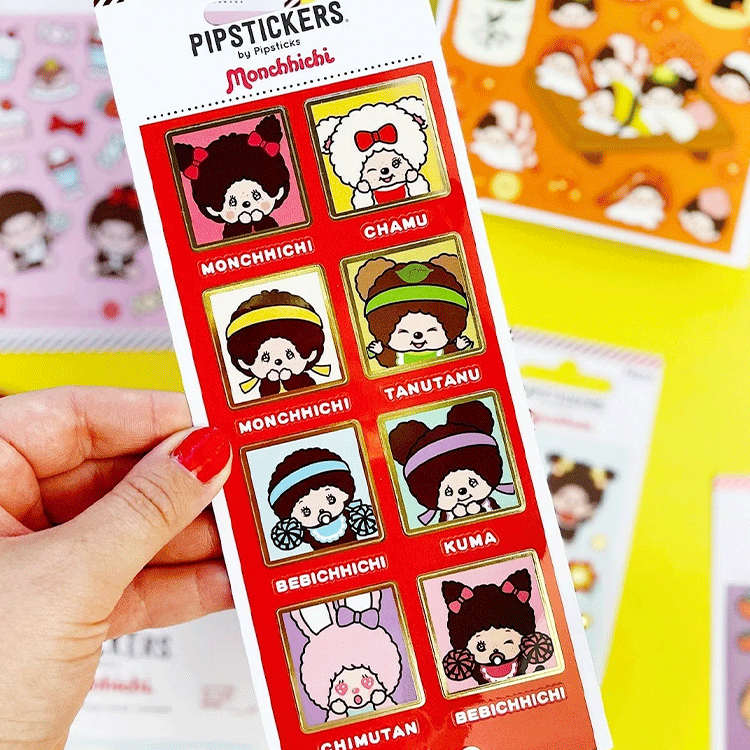 Hand holding PipSticks Monchhichi collection sheet with kawaii character portraits and gold foil accents on red border