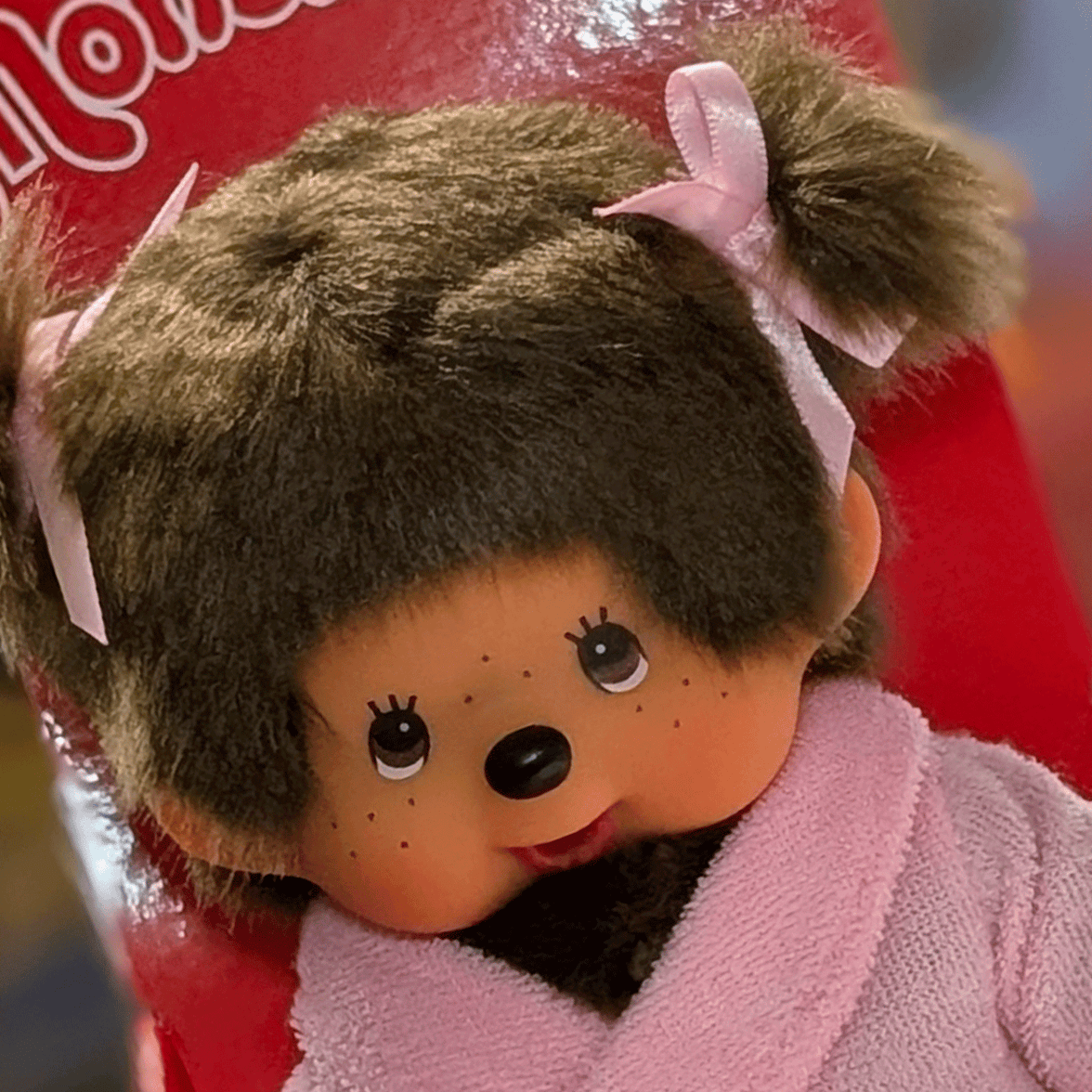 Sekiguchi 8-inch Monchhichi girl doll with brown fur and pink bathrobe on red background