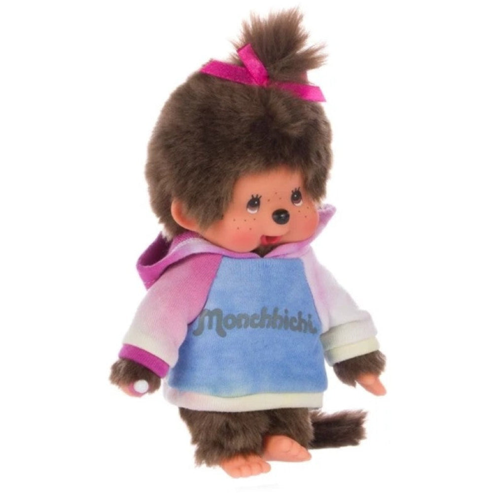 A plush toy doll with brown fur, a pink bow, and a pastel pink, purple, and blue hoodie with 'Monchichi' written on the front, shown against a plain white background.