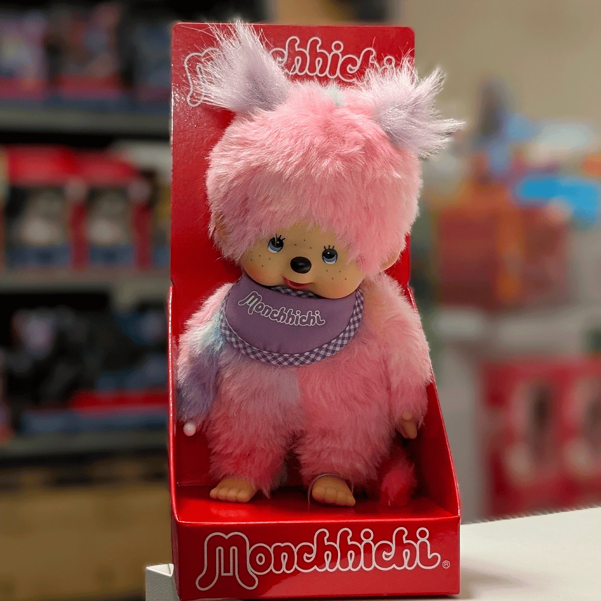 Sekiguchi 8-inch Monchhichi girl plush doll with pink tie-dye fur and purple bib in red display packaging