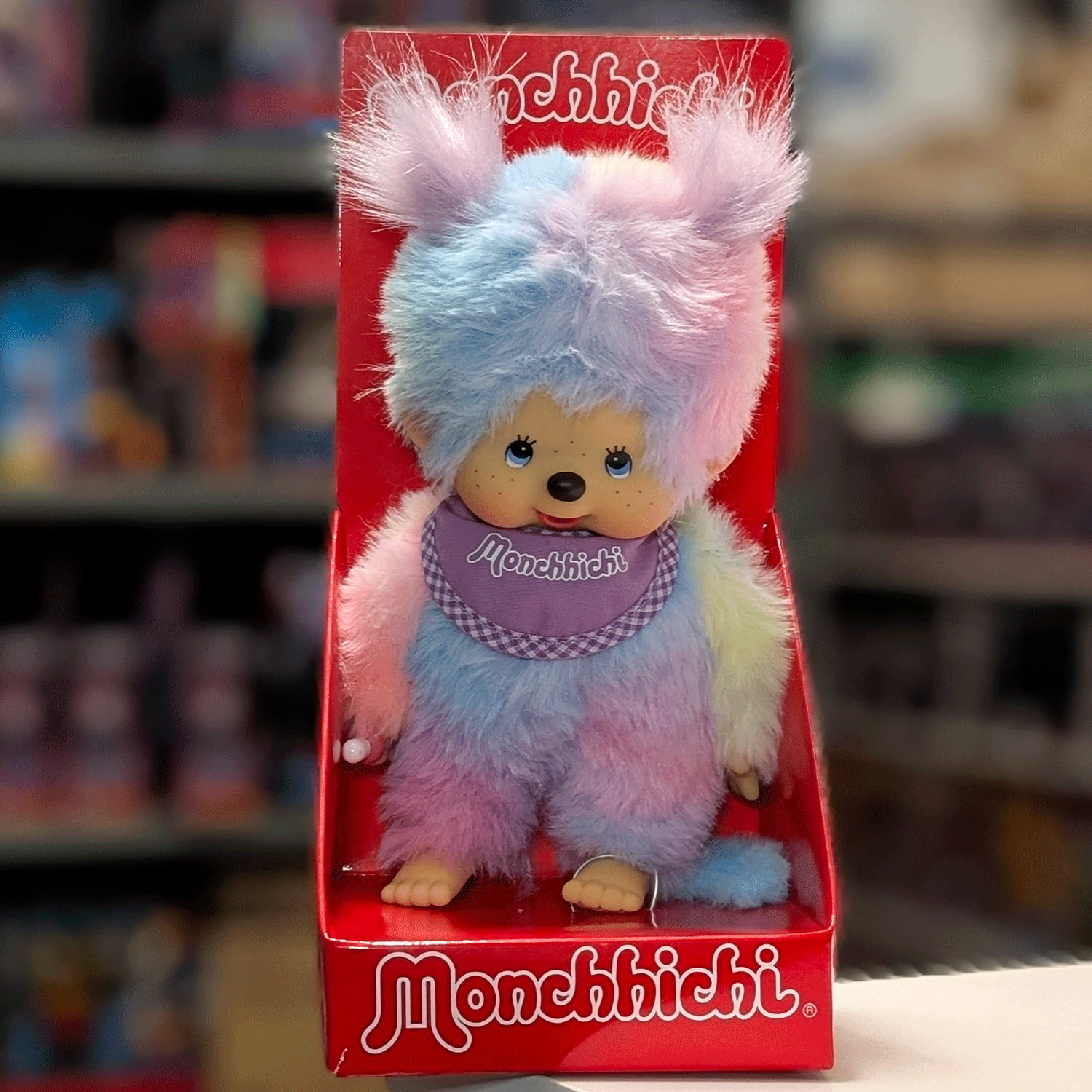 Sekiguchi 8-inch Monchhichi girl plush doll with multicolor pastel tie-dye fur and purple bib in red display box