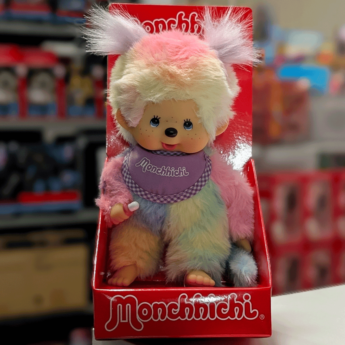 Sekiguchi 8-inch Monchhichi girl plush doll in pastel tie-dye fur wearing purple bib seated in red box