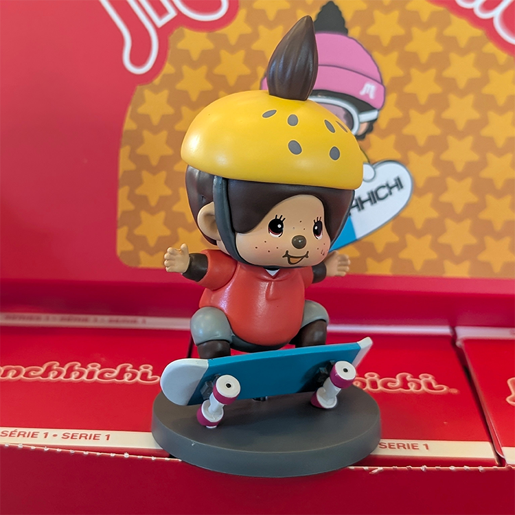 Sekiguchi Monchhichi vinyl figure of a boy skateboarder with yellow helmet and red shirt on grey stand