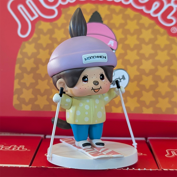 Sekiguchi Monchhichi vinyl figure skiing in yellow jacket and purple hat on white stand with red background packaging.