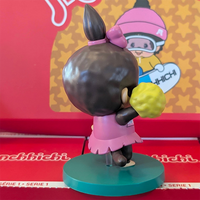 Sekiguchi Monchhichi Girl Cheerleader vinyl figure in pink outfit holding yellow pom-poms on green stand.