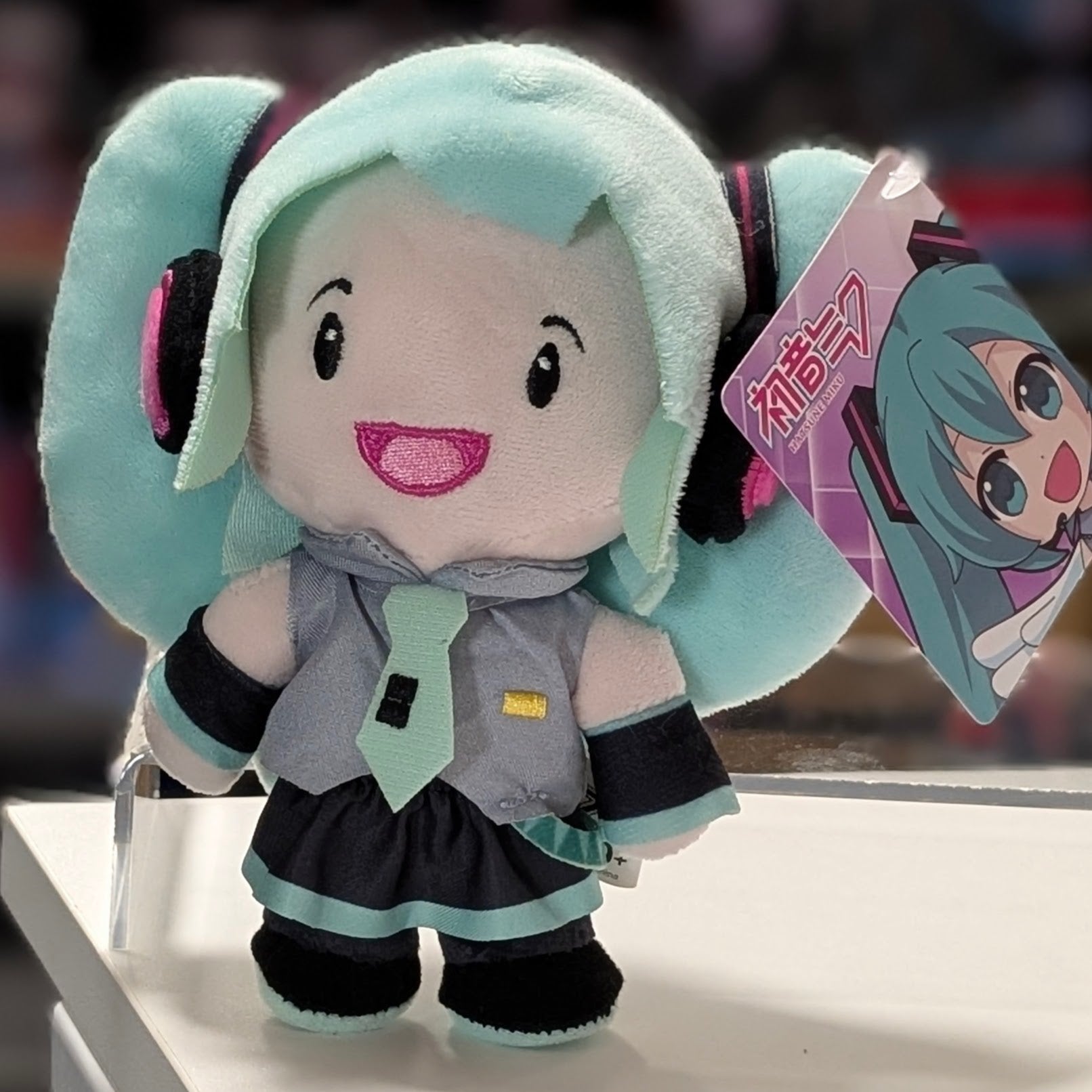 UCC 6-inch Hatsune Miku plush with teal twin tails, smiling face, gray outfit, and attached character tag