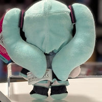 Rear view of UCC branded 6-inch Hatsune Miku plush with twin teal ponytails and care label displayed on a white surface