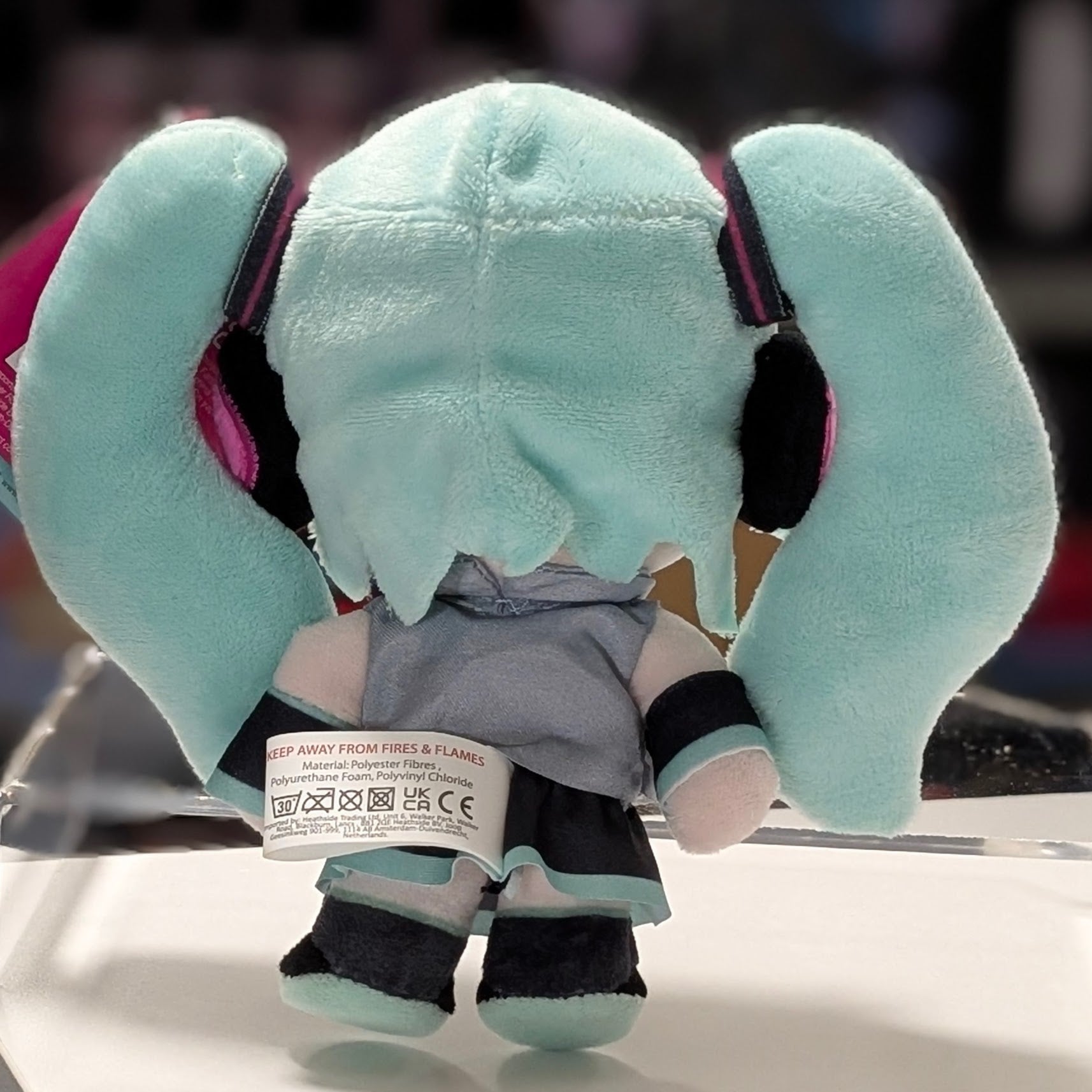 Rear view of UCC 6-inch Hatsune Miku plush showing teal twin tails and gray outfit with care label visible