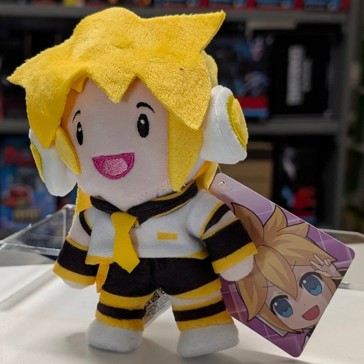 UCC 6-inch Kagamine Len plush with yellow hair, white headphones, black and yellow outfit smiling with tag on clear display stand