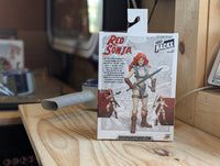 Action figure packaging with 'Red Sonja' on a wooden surface