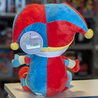 Rear view of a soft plush toy in bright red and blue colors wearing a jester-style hat with yellow pom-poms