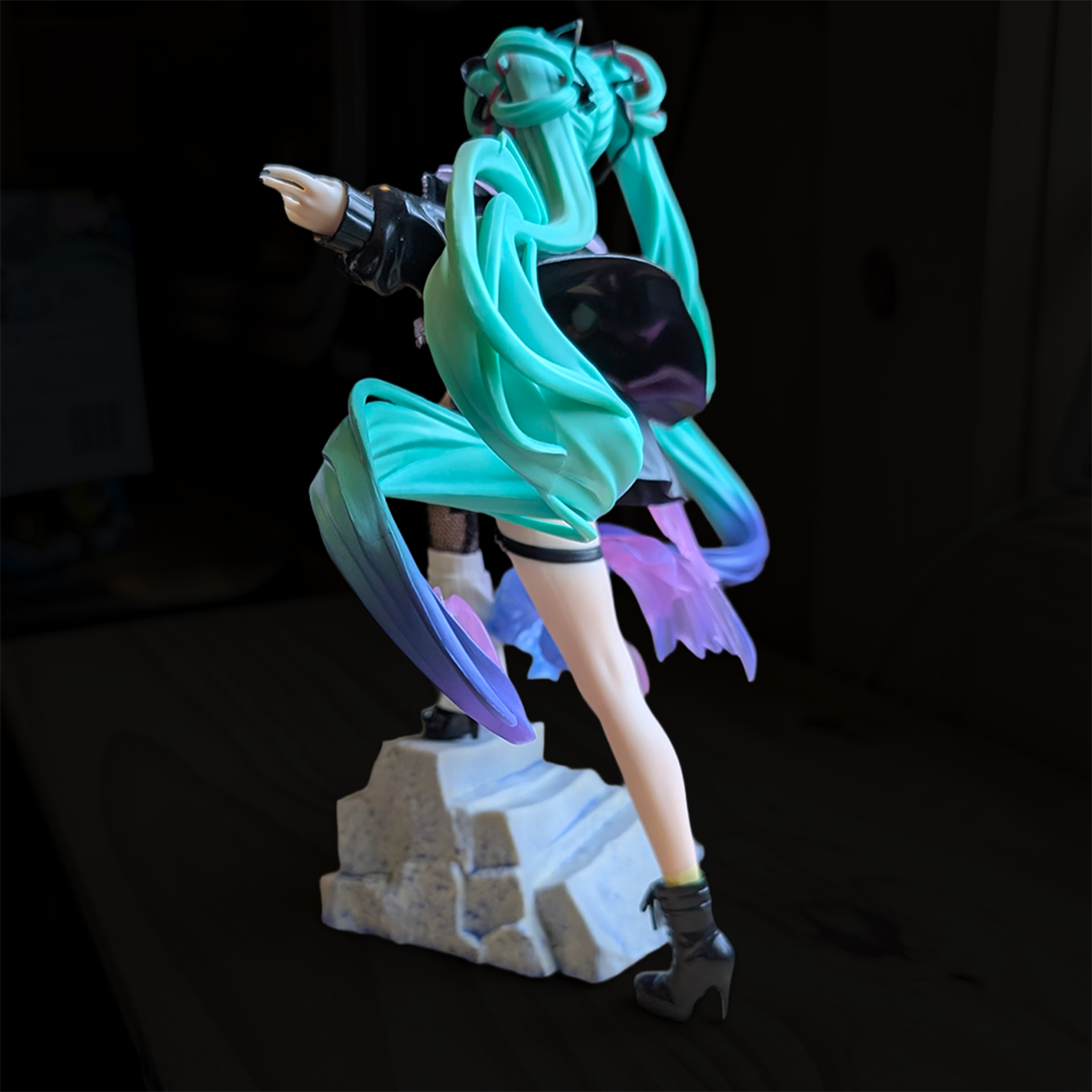 Figure with long teal twin tails and black outfit posed on stone-like base against dark background