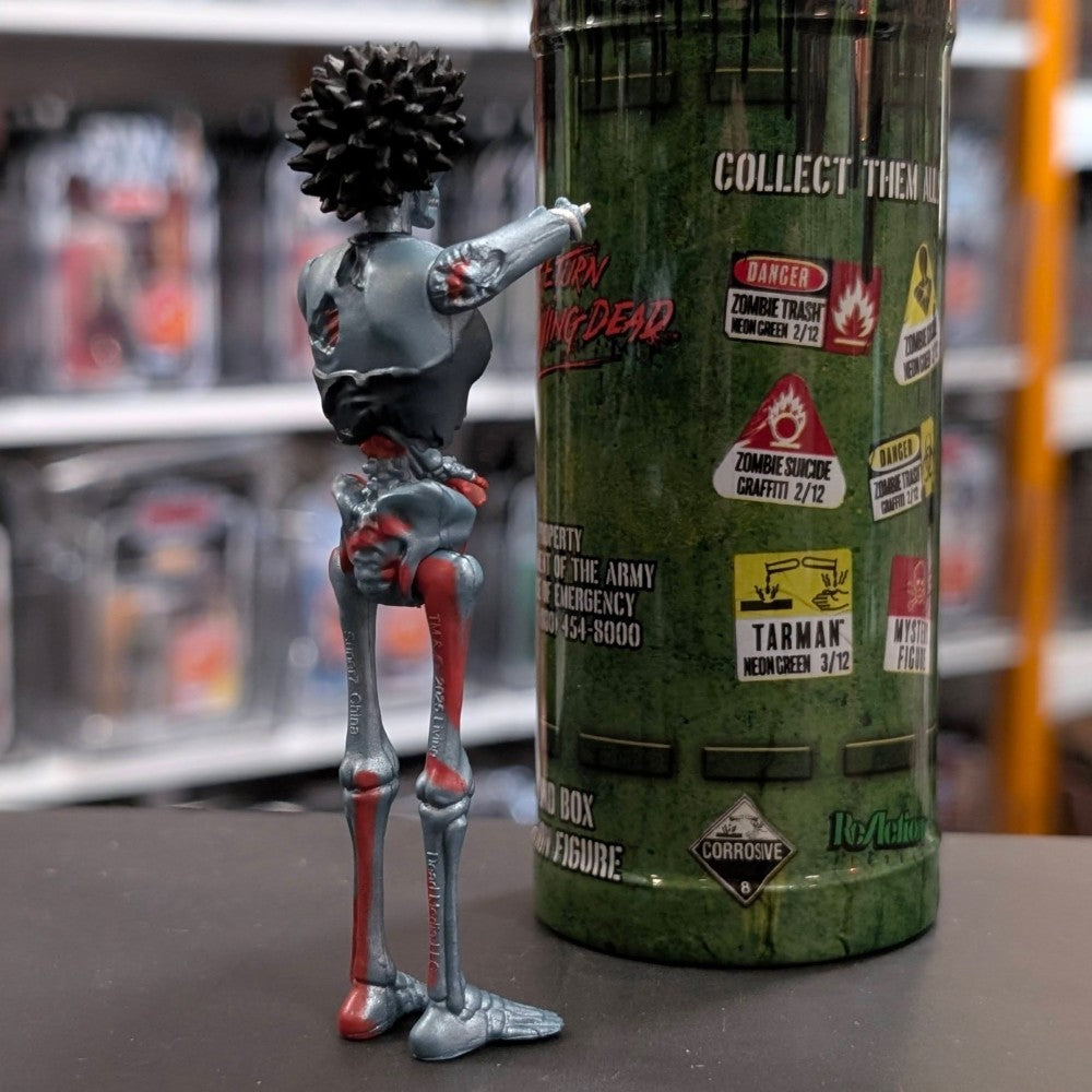 Super7 metallic blue female zombie figure with spiked hair posed beside green Return of the Living Dead collectible tube