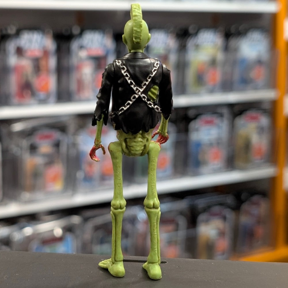 Super7 neon green male zombie figure with mohawk, black jacket with chains, and exposed skeletal details viewed from behind